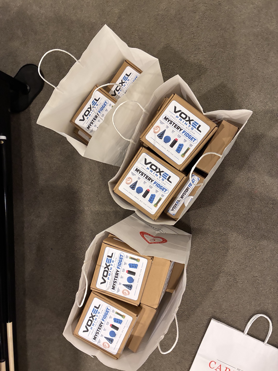 Brown Voxel Prints Mystery Fidget boxes with white-and-blue labels, packed in paper shopping bags.